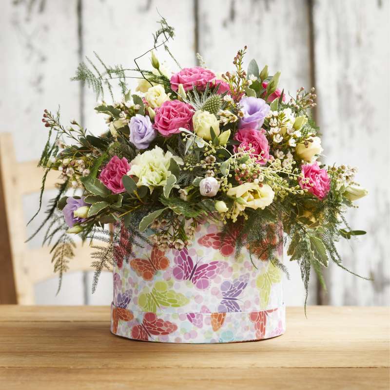 Carnations, spray roses and plenty of foliage in a colourful, butterfly-themed hat box Valentines arrangement.