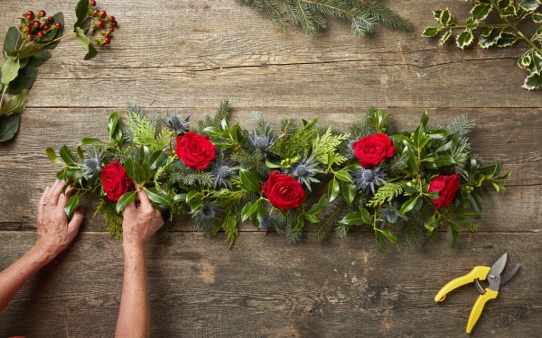 Adding red roses to a DIY fresh Christmas garland.