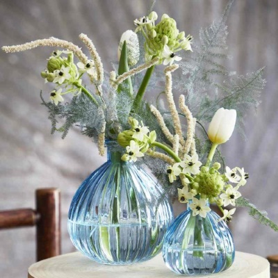 Two clear, blue, rounded vases of different sizes. Each vase features similar, easy DIY floral arrangements with white tulips and foliage. 