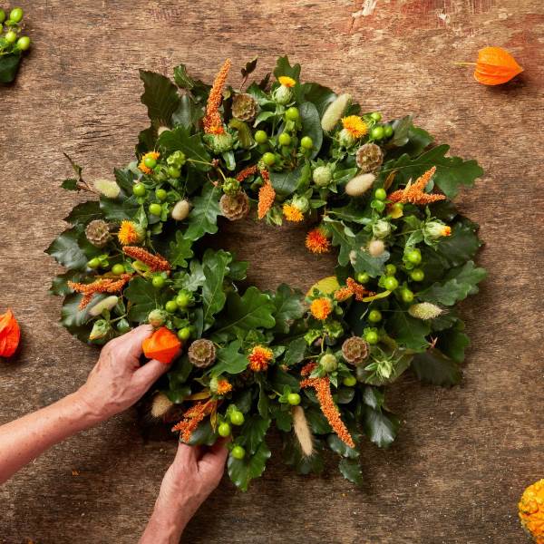 Adding orange, brown and green flowers and foliage to a Halloween floral wreath