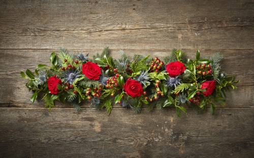 Finished festive floral garland with green foliage, thistles, pine tree leaves, red berries and red roses.