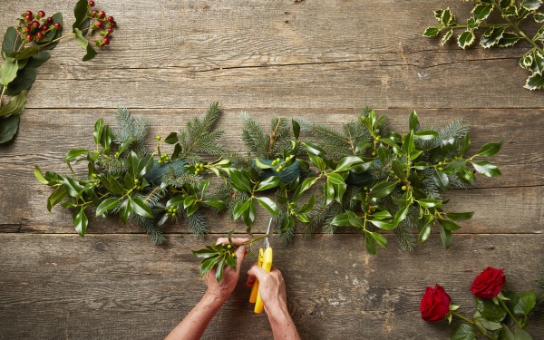 Cutting and inserting foliage into a fresh festive floral garland.