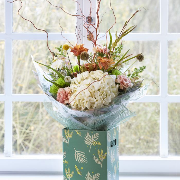 Teal floral box with beautiful, earthy-toned floral arrangement featuring cream hydrangeas front and centre.