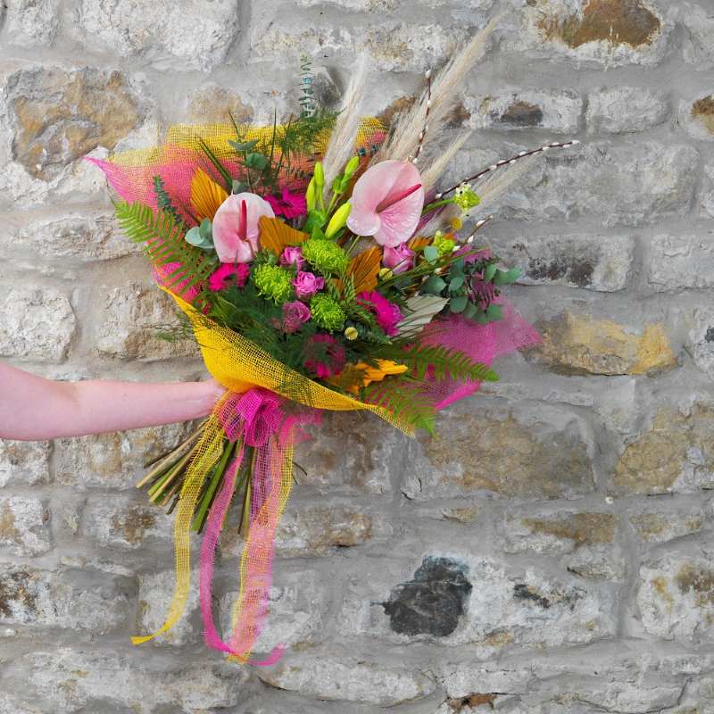 Colourful floral bouquet with closed lilies, opened lilies, pink roses, green foliage and more. It is tied together with a pink and yellow jute fibre wrap.