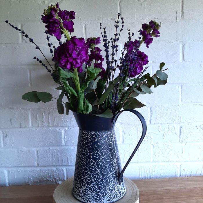 Purple lavender and green foliage in a charcoal grey flower jug with white pattern.
